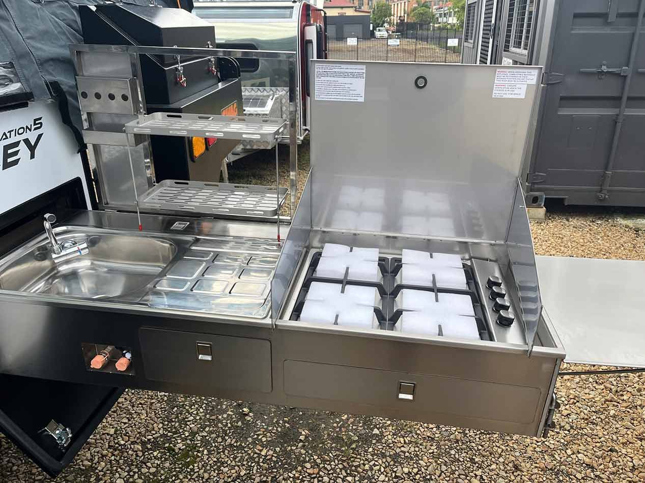 A Stainless Steel Kitchen With A Sink, Stove And Drawers Attached To A Trailer — Perkins Caravans in Ballina, NSW