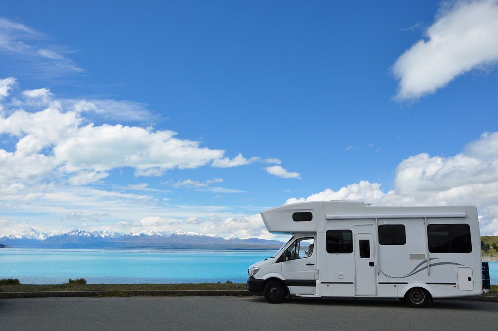 A White RV Is Parked On The Side Of The Road Next To A Lake — Perkins Caravans in Yamba, NSW