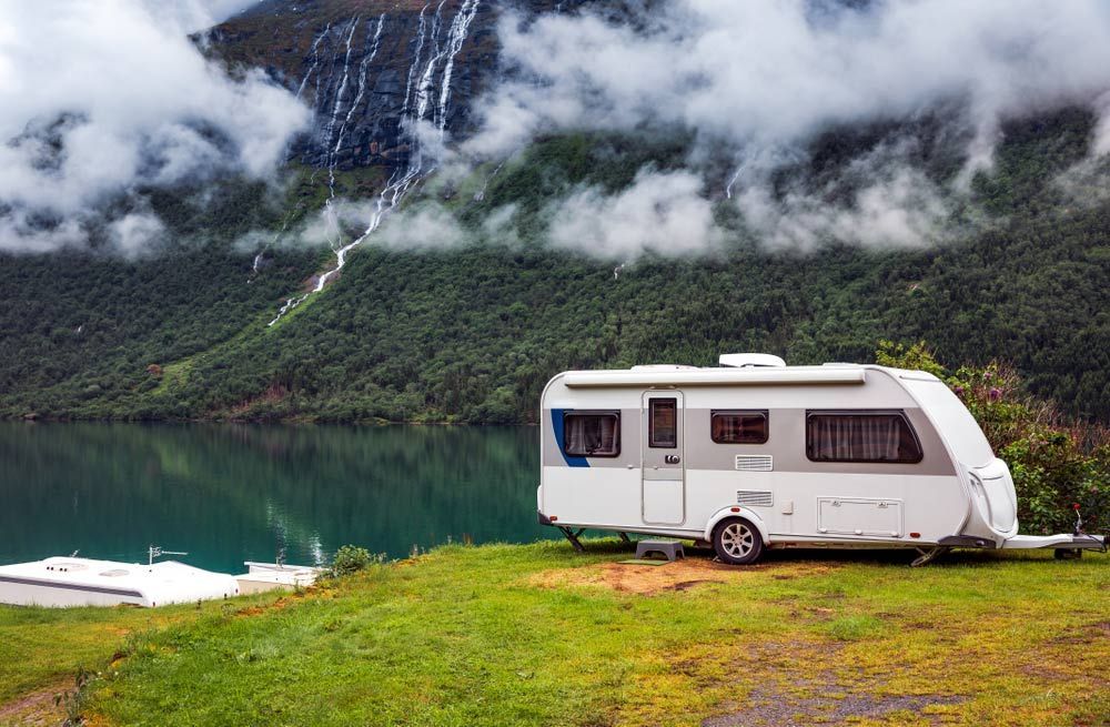 A Camper Is Parked On A Grassy Hill Next To A Lake — Perkins Caravans in Byron Bay, NSW