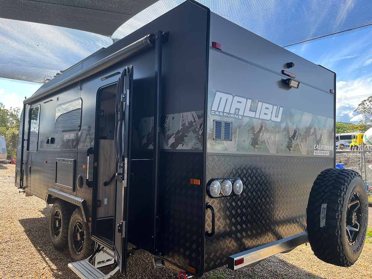 A Black Camper Trailer Is Parked In A Gravel Lot — Perkins Caravans in Yamba, NSW