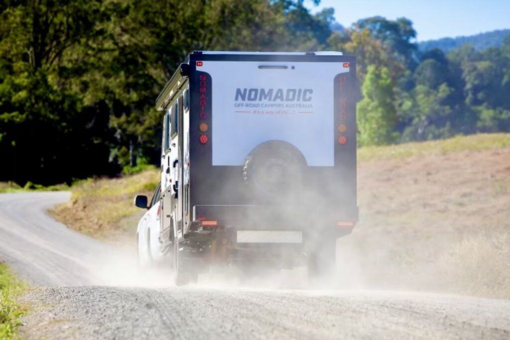 A Car Is Driving Down A Dirt Road With To A Caravan On The Back — Perkins Caravans in Ballina, NSW