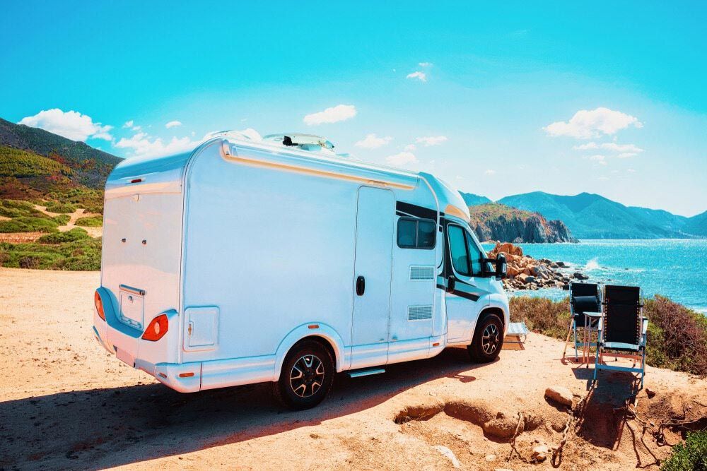 A White RV Is Parked On A Dirt Road Next To The Ocean — Perkins Caravans in Ballina, NSW