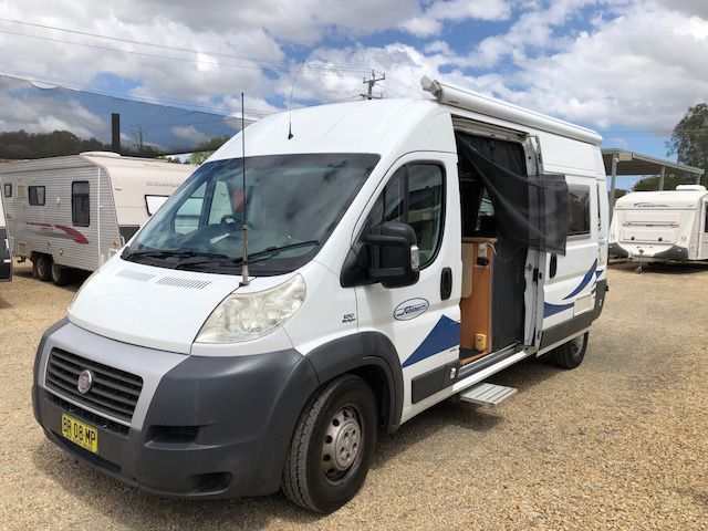A White Van With The Door Open Is Parked In A Gravel Lot — Perkins Caravans in Byron Bay, NSW