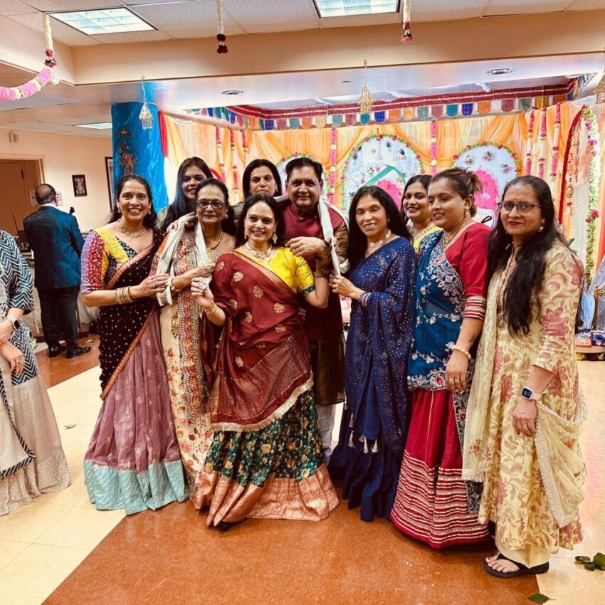 Group of people in traditional clothing pose for a photo at an event, colorful decorations in the background.