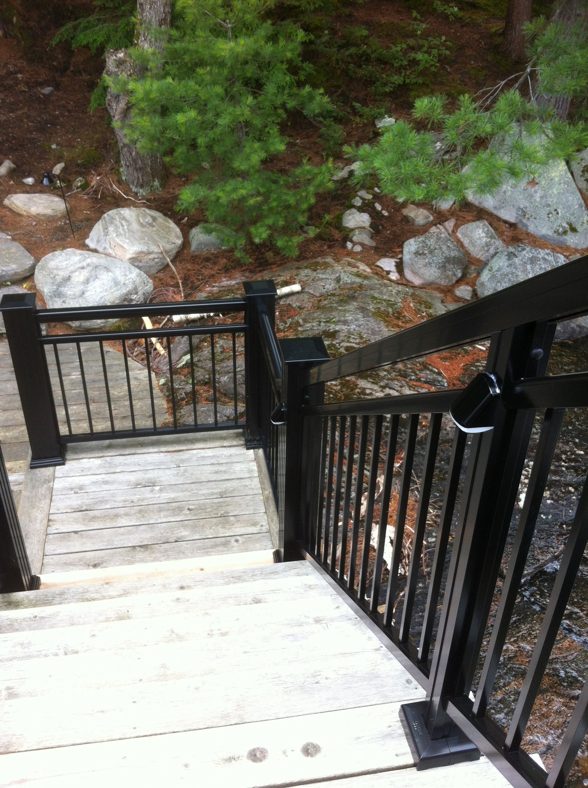 A set of stairs with a black railing leading to a rocky area by Premier Decks & Awnings