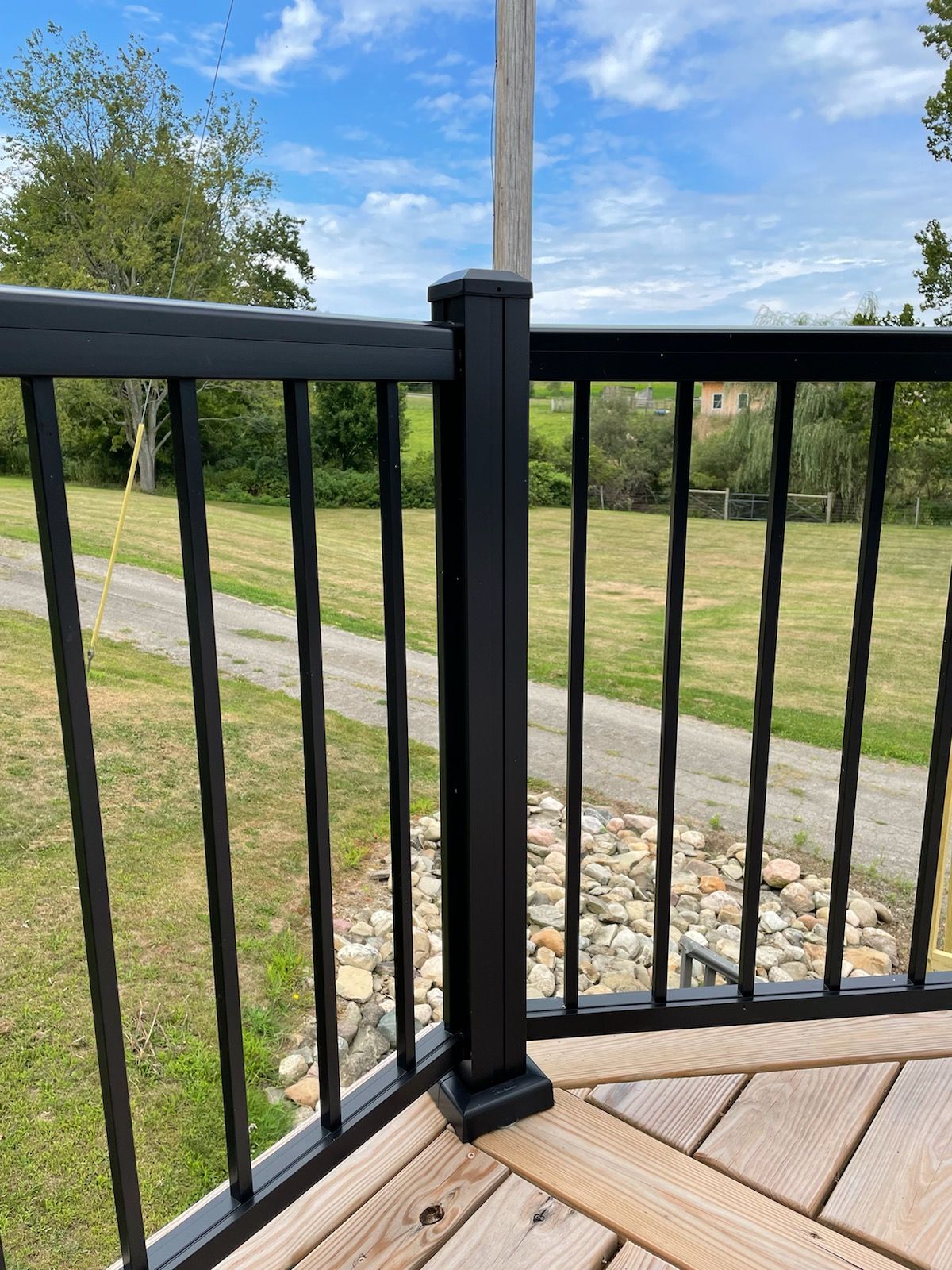A black railing on a wooden deck with a field in the background