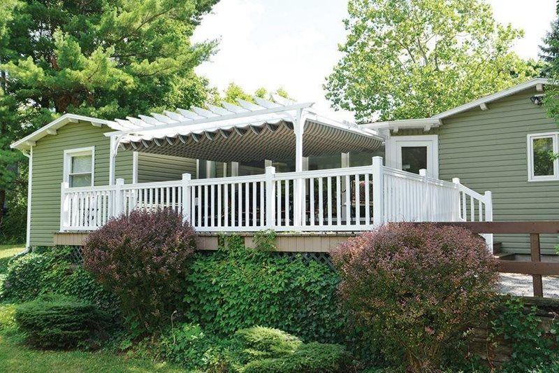 A green house with a white deck and pergola