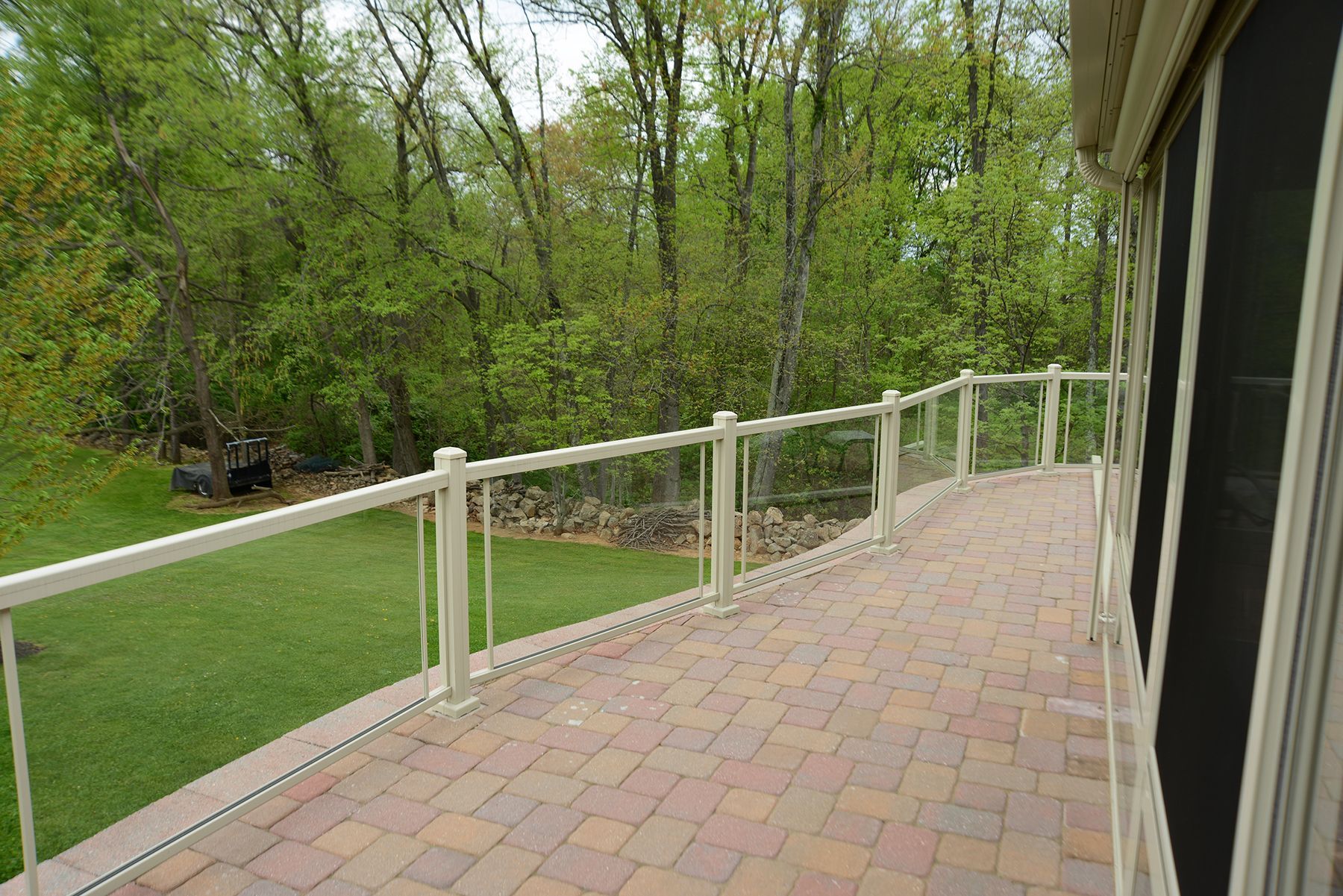 A brick deck with a glass railing overlooking a lush green field by Premier Decks & Awnings