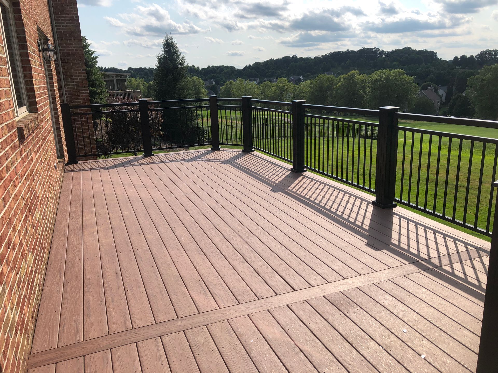 A wooden deck with a black railing and a brick building in the background