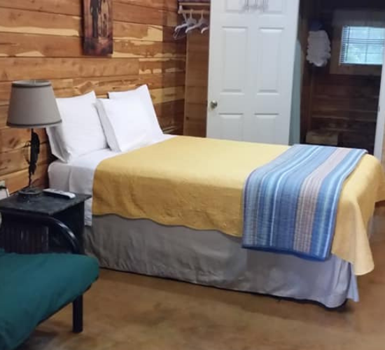 Rustic bedroom with a bed, yellow blanket, blue striped throw, lamp, and chair