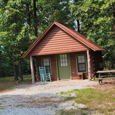 Small rustic cabin with green door and blue rocking chair in a wooded clearing
