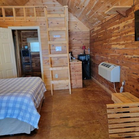 Cozy wood-paneled bedroom with loft ladder, bed, dresser, wall heater, and bench chair