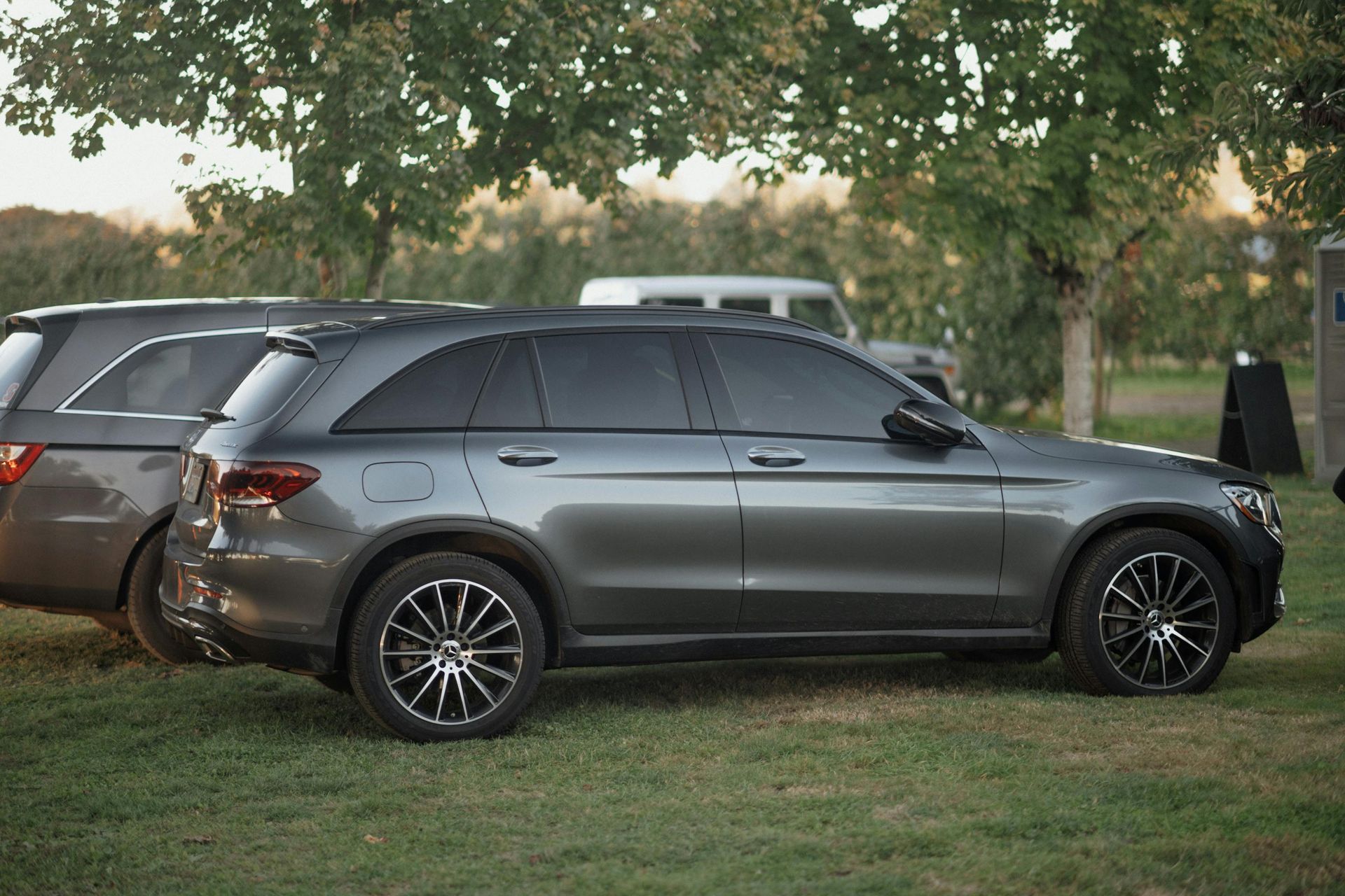 A gray suv is parked in a grassy field next to a trailer.