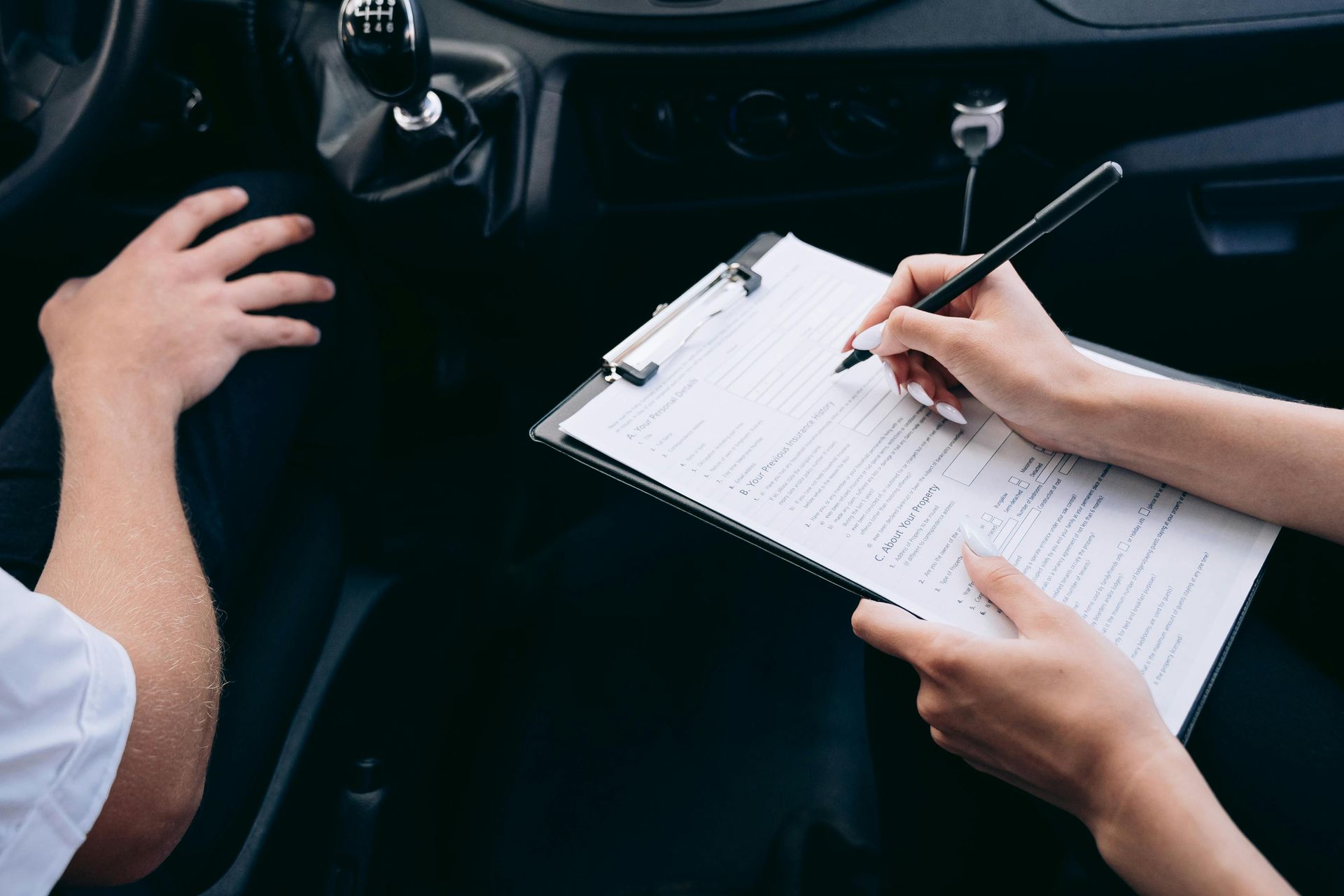 A person is sitting in a car writing on a clipboard.