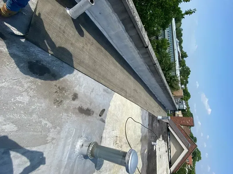 Flat roof with vent pipes and a parapet wall against a blue sky, sunlight reflecting.