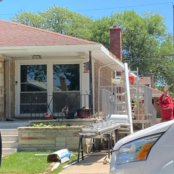 House exterior with a person working on a ladder. White siding, brown roof, and brick.
