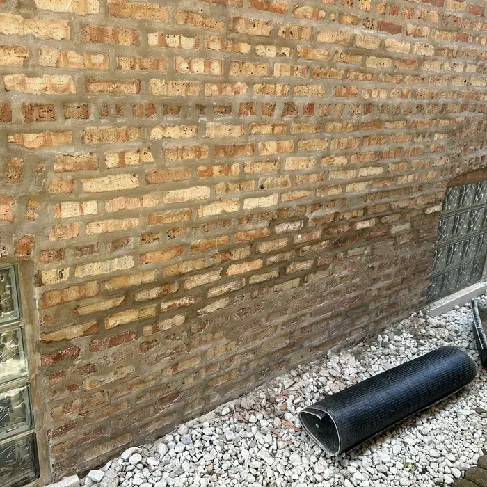 Brick wall with glass block window, drainage pipe, and gravel base.