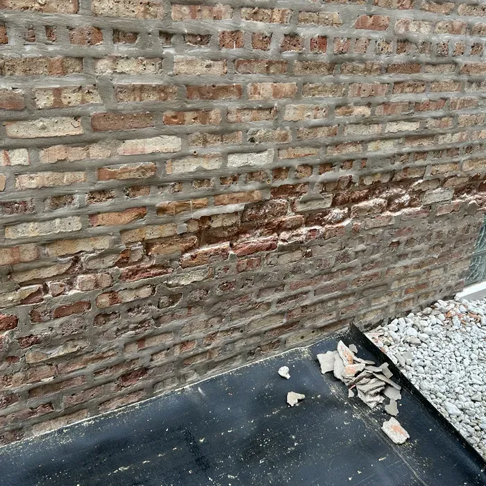 Damaged brick wall with crumbling bricks and mortar, resting on a black surface with debris.