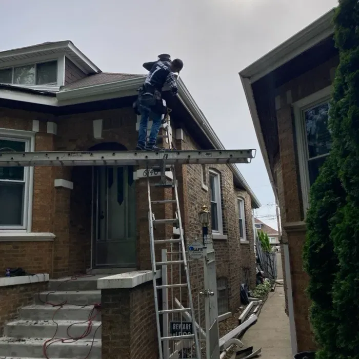 Two workers on a ladder, installing a gutter on a brick house. Overcast sky.