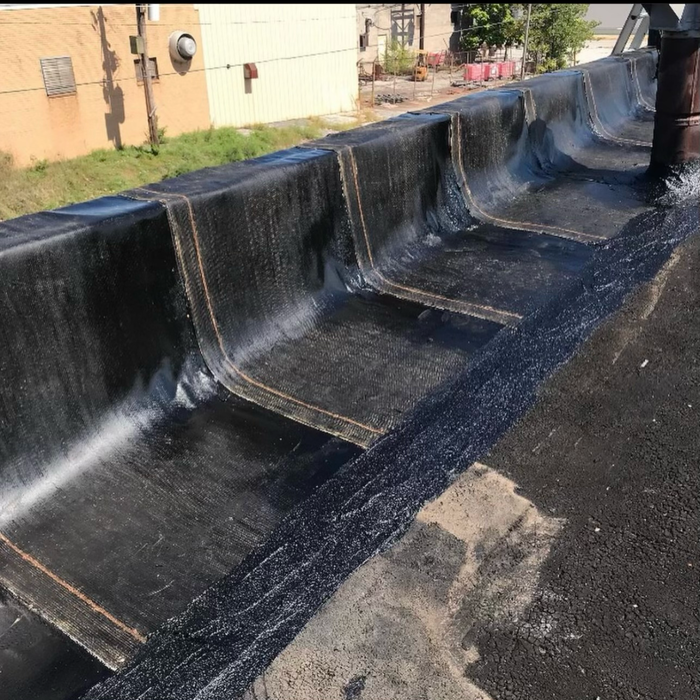 Flat roof with black sealant and a built-in trough. A building and vegetation are visible in the background.