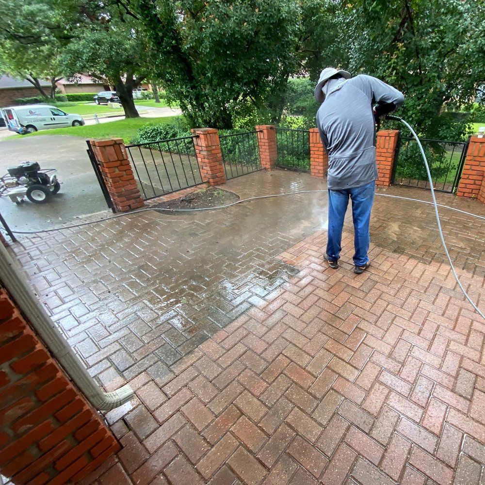 Person pressure washing a brick patio. The cleaned area is lighter than the unwashed section.