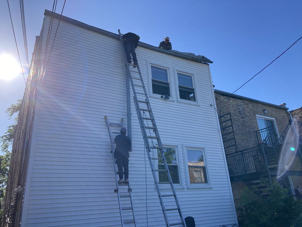 Two people on a roof, one on a ladder. White building with blue sky background.