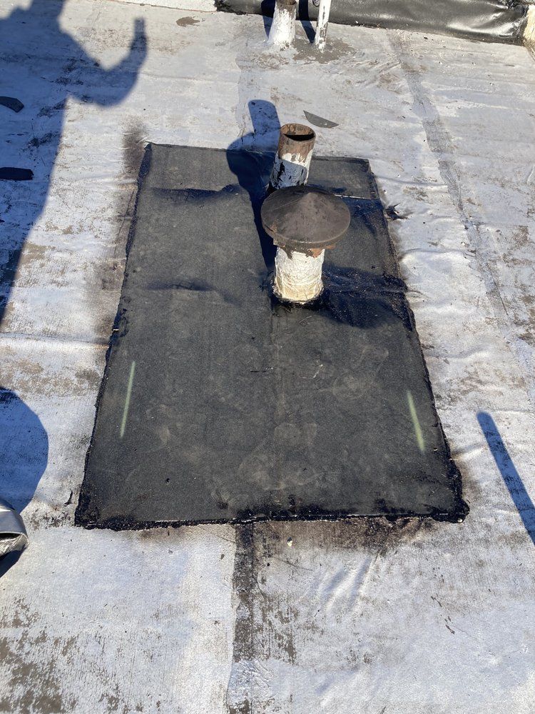 Black roofing material with a vent pipe and chimney on a flat roof.