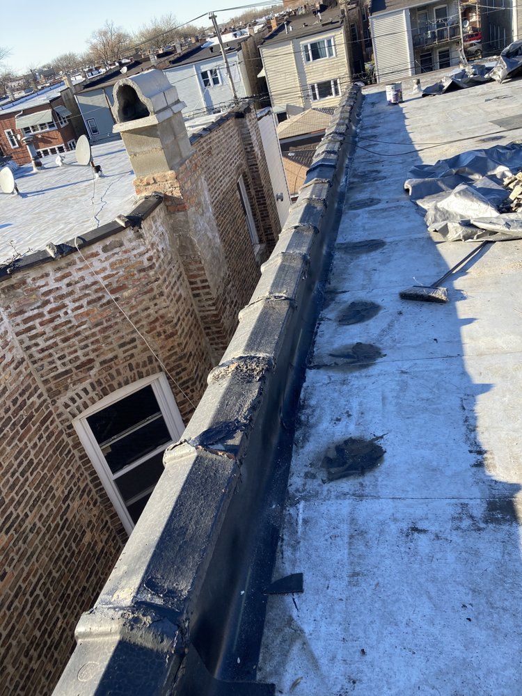 Rooftop view of a building with a brick wall, chimney, and a dark-colored ledge. Blue sky.