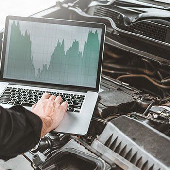 Person on a laptop under the hood of a car