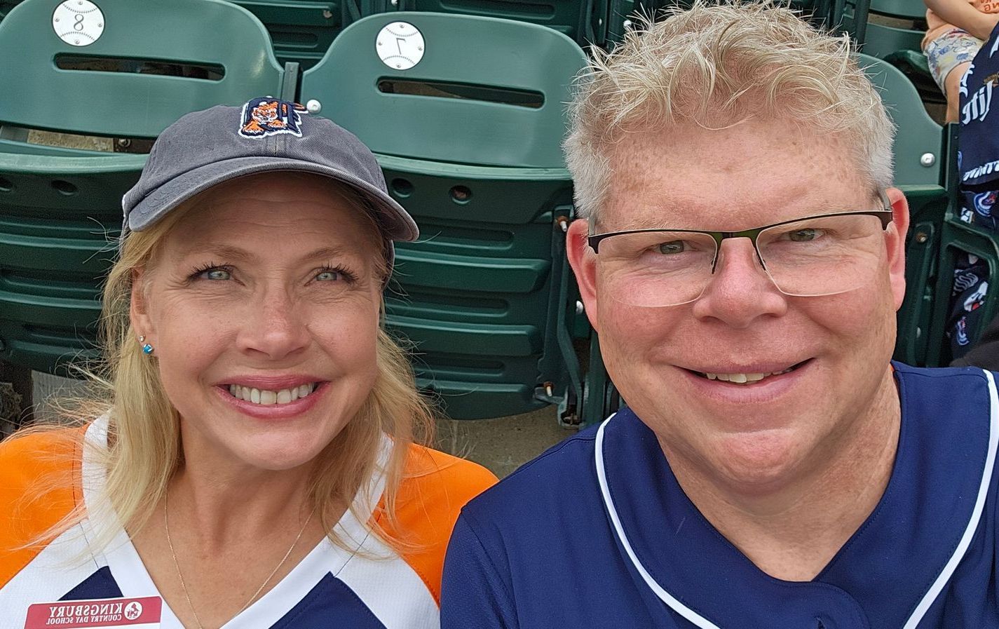 Adam Stewart and his wife are posing for a picture in a baseball stadium.