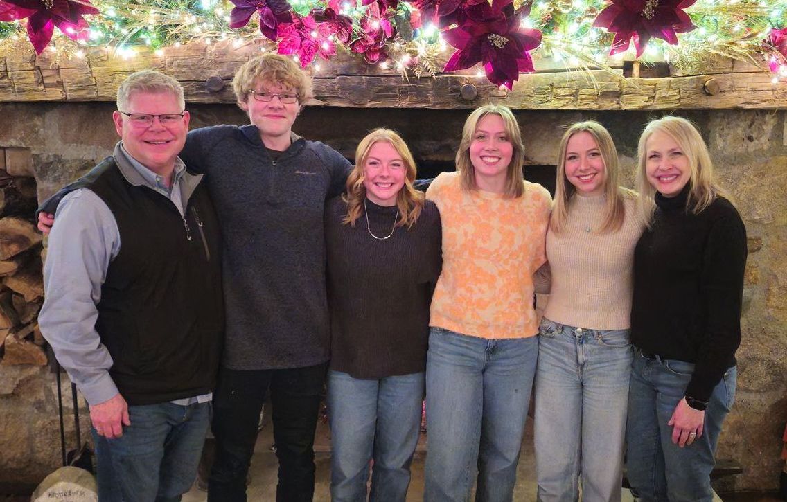 Adam Stewart and his family is posing for a picture in front of a fireplace at Christmas