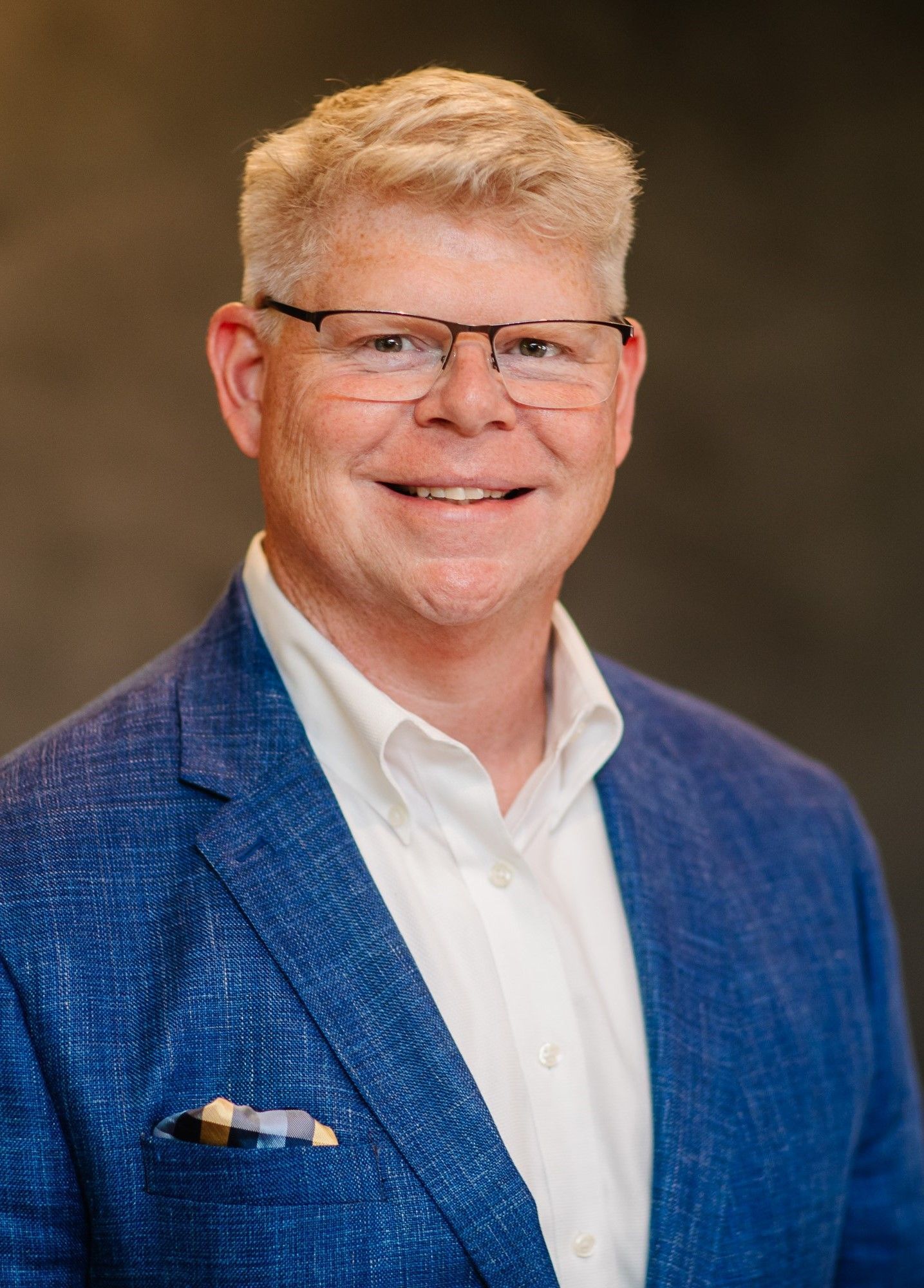 Founder Adam Steward wears glasses and a blue jacket and smiles for the camera.
