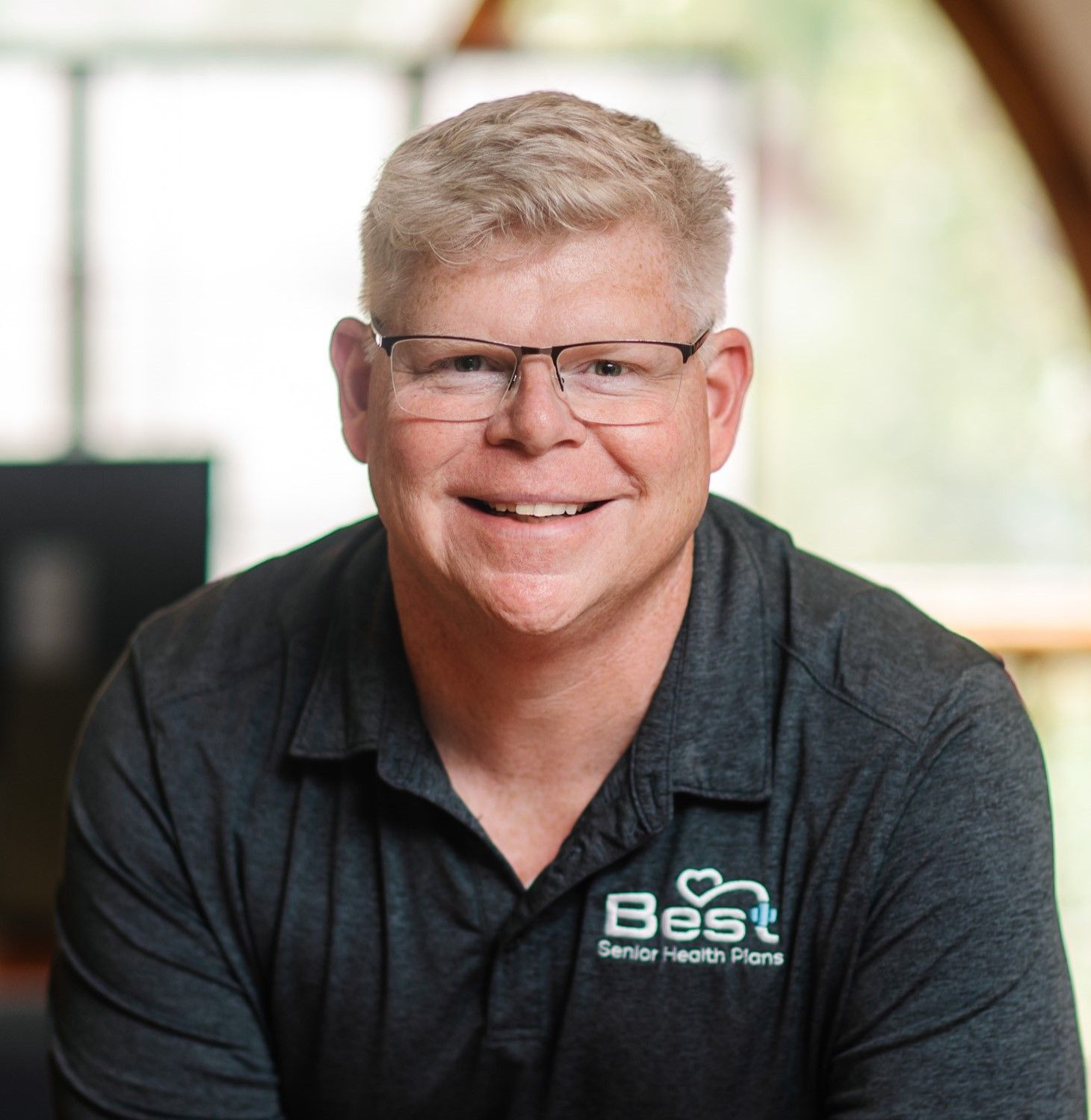 Adam Stewart, agency founder, wears glasses and a shirt that says Best Senior Health Plans on it