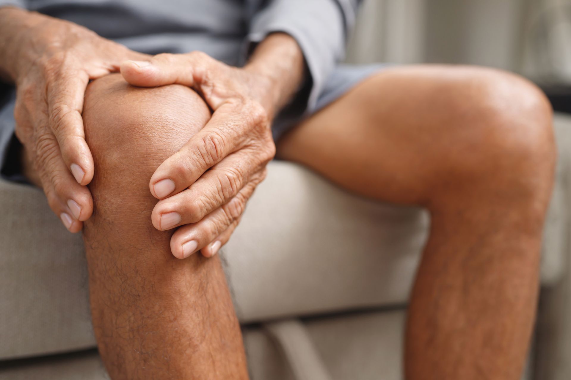 A man is sitting on a couch holding his knee in pain.