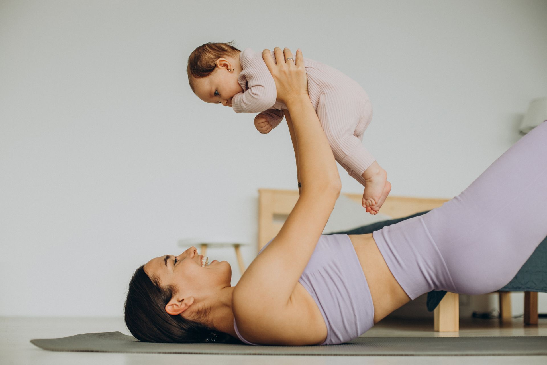 A woman is laying on a yoga mat holding a baby in her arms.