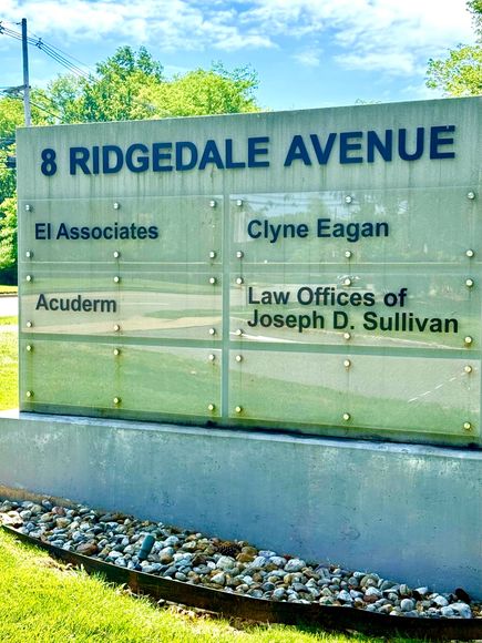 Glass sign for 8 Ridgedale Avenue listing office names against a blue sky.