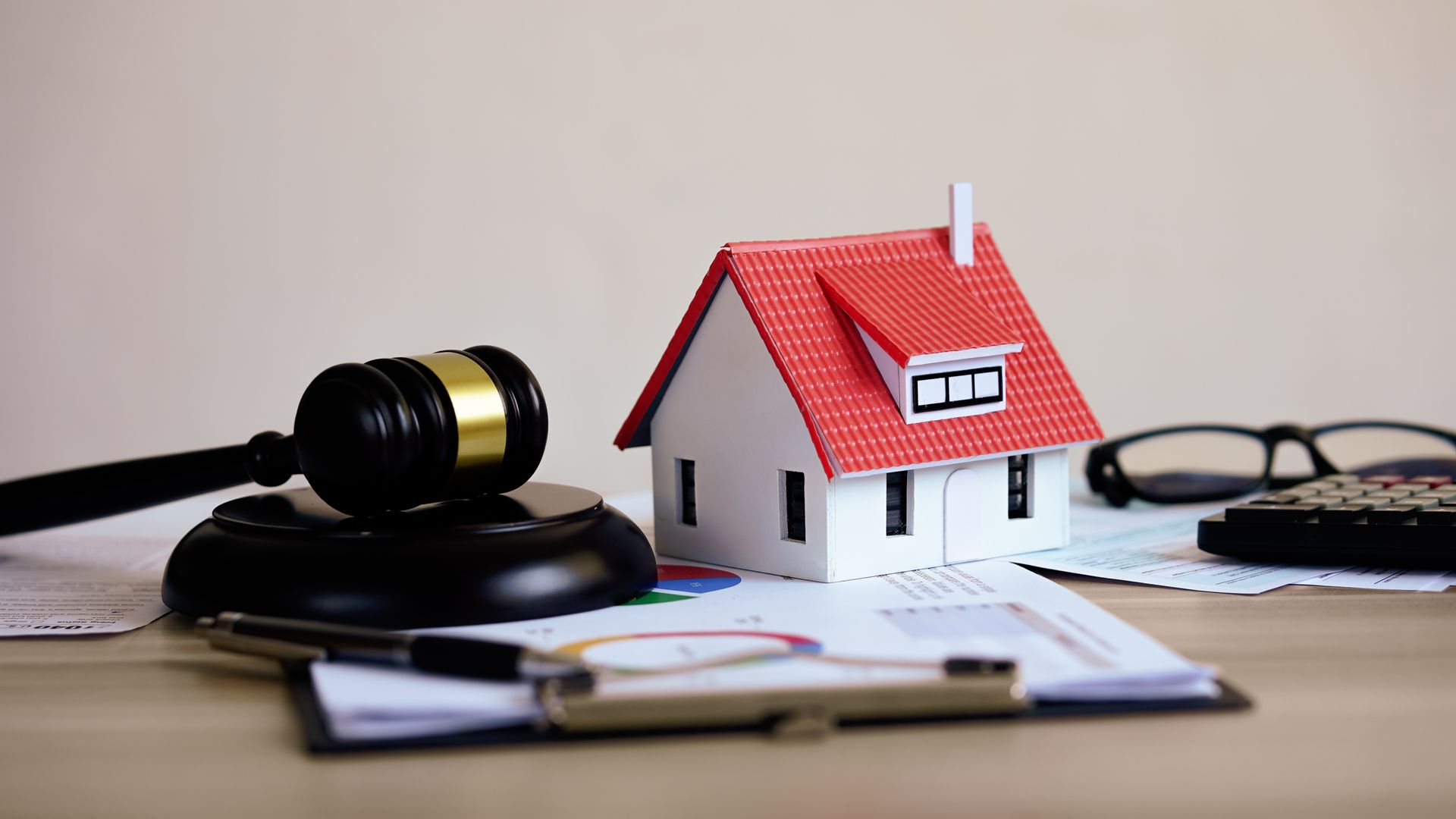 House model with red roof beside a judge’s gavel, papers, and eyeglasses on a desk