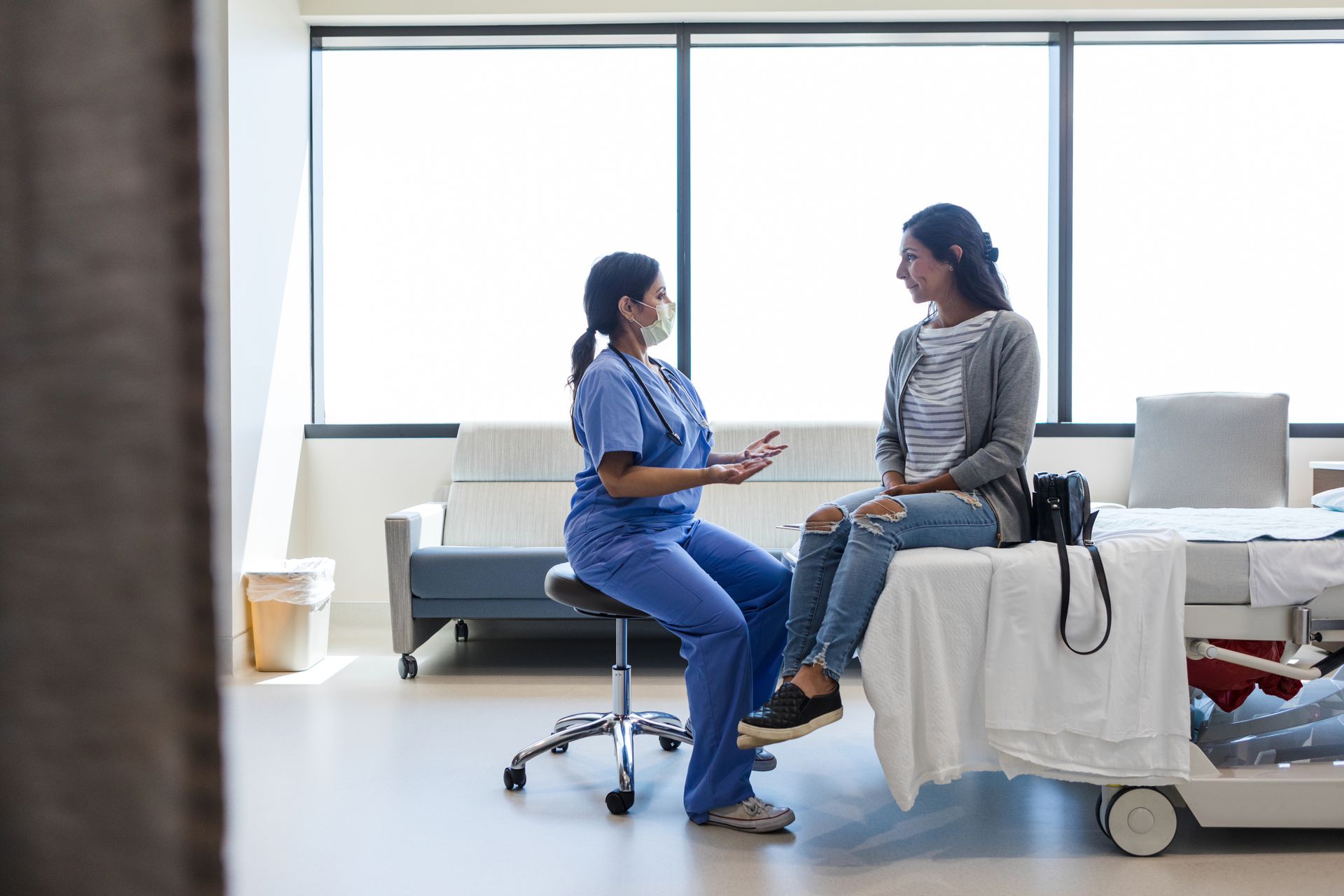 A nurse is talking to a patient sitting on a hospital bed.