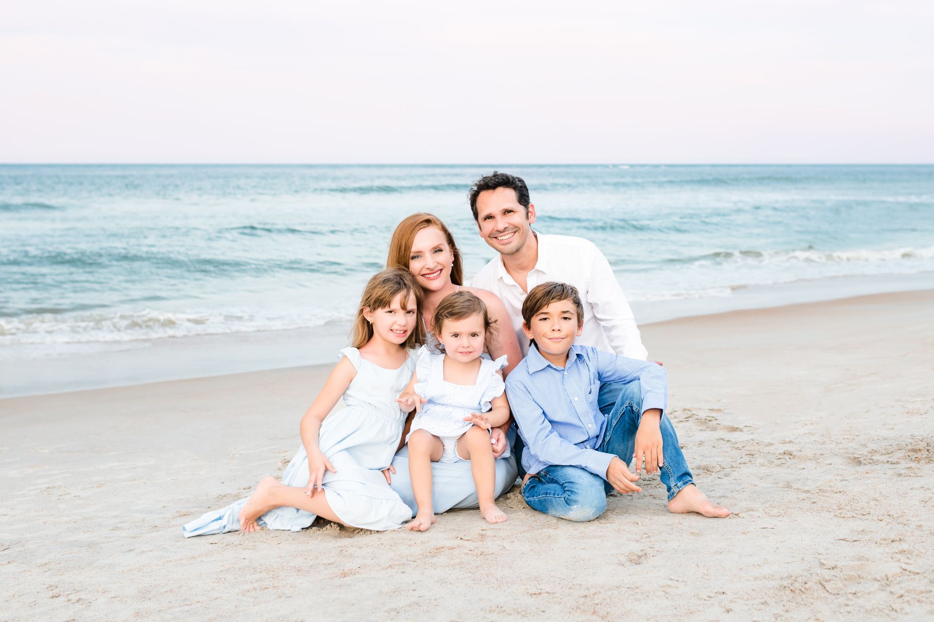 A family is sitting on the beach posing for a picture.