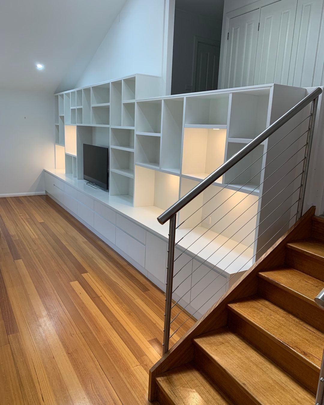 A Living Room With Hardwood Floors , White Shelves and Stairs — Stephen Veigel Kitchens In Gosford, NSW