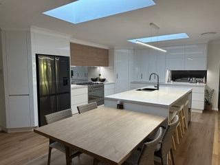 Modern kitchen with white cabinetry, island, and dining table; black refrigerator, skylights, wooden floors - Stephen Veigel Kitchens In Gosford, NSW