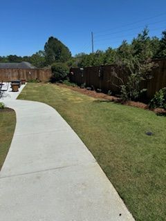 A Concrete Walkway Leading to a Lush Green Yard With a Wooden Fence