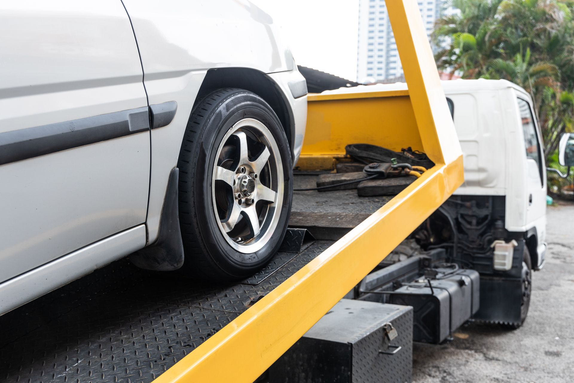 Silver car loaded on a tow truck ramp with yellow support beams, viewed from the side