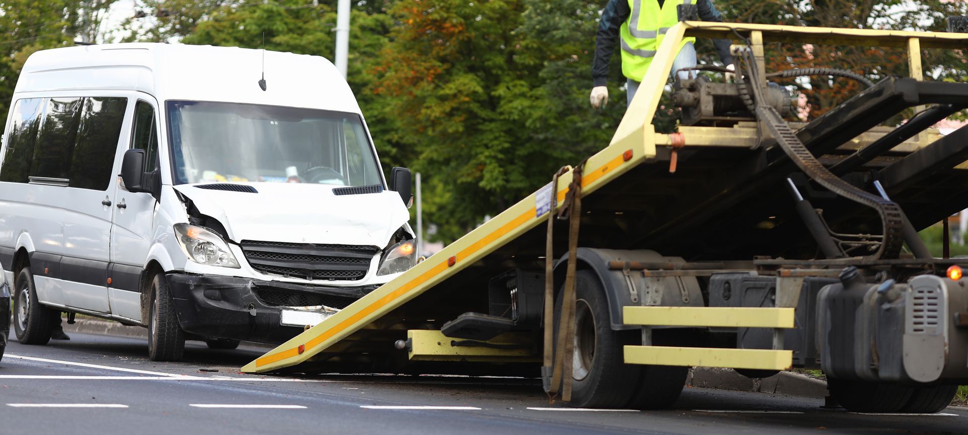 Damaged white van and tow truck with tilted ramp after roadside collision