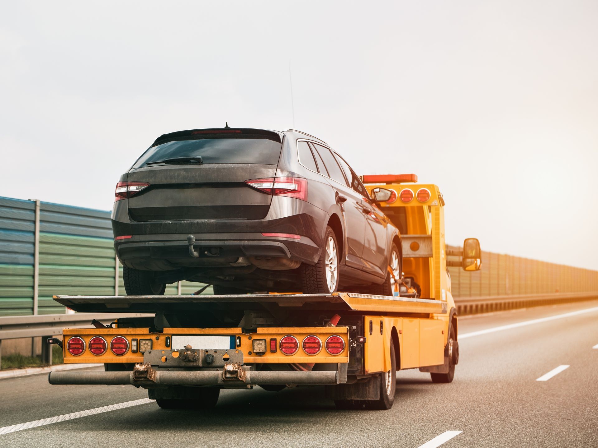 Black SUV on a tow truck driving on a highway at sunset