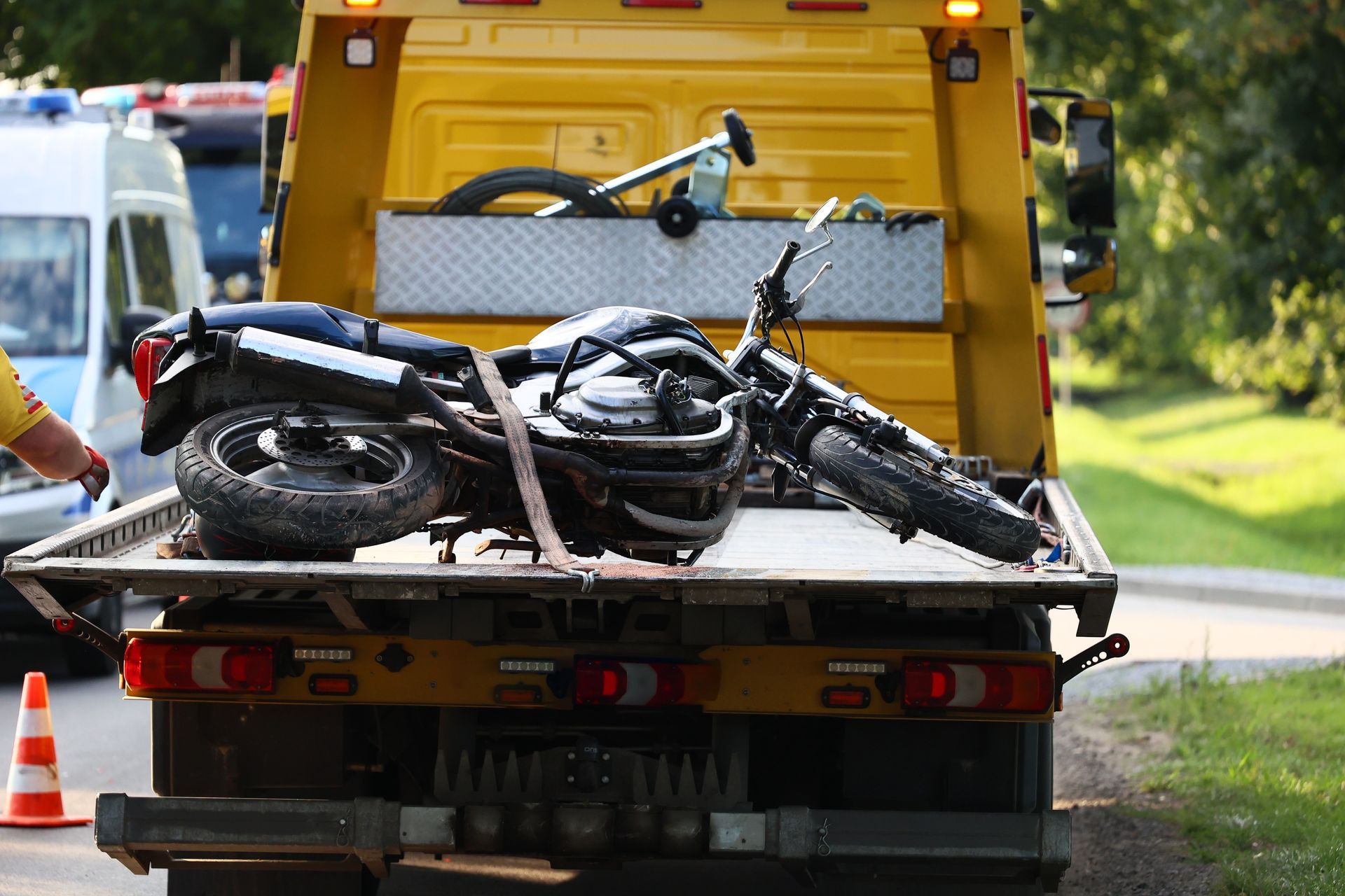 Tow truck carrying a tipped black motorcycle on a flatbed by the roadside