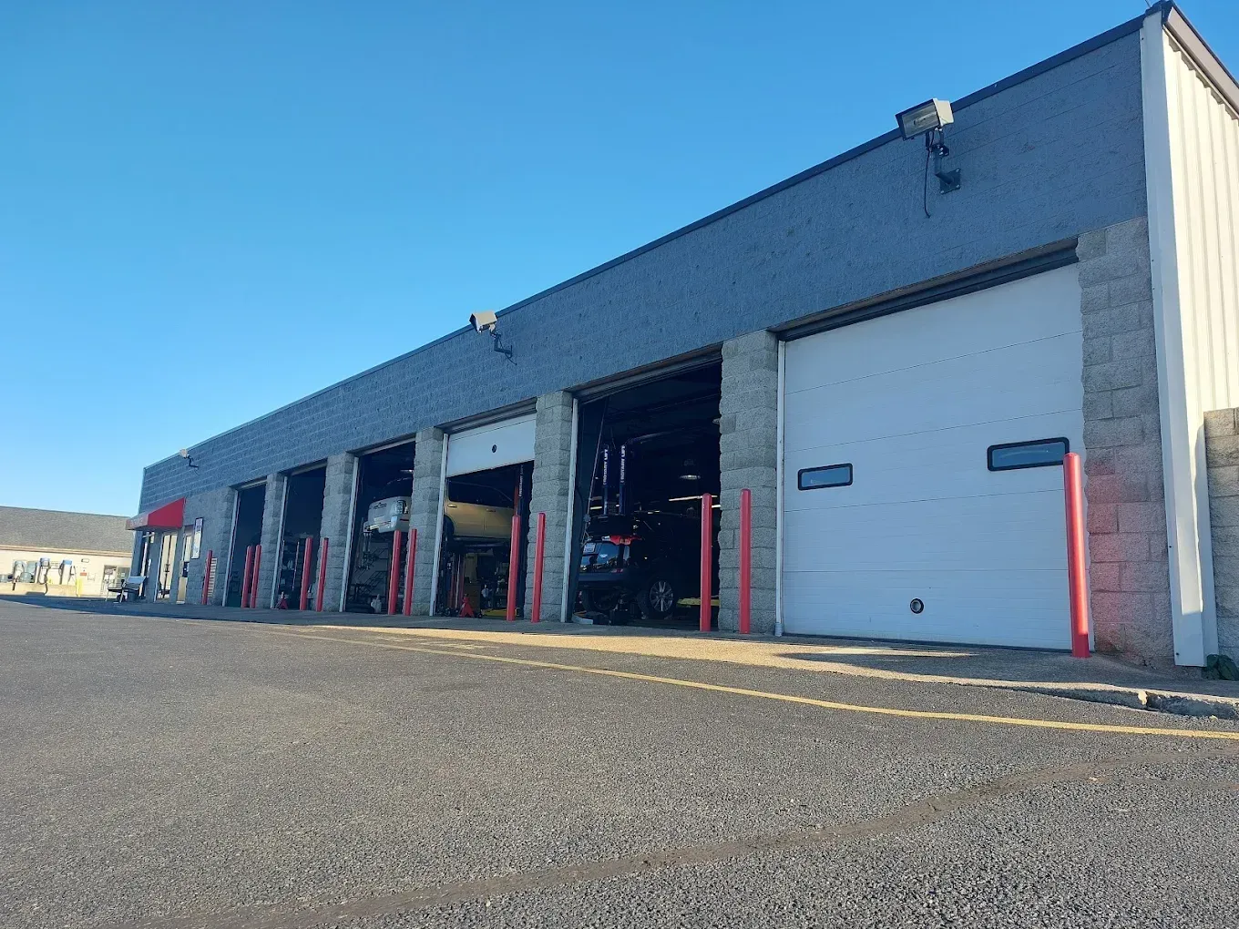 A row of garage bays with closed and open white doors, exterior view. Gray building, gravel lot, and clear blue sky.