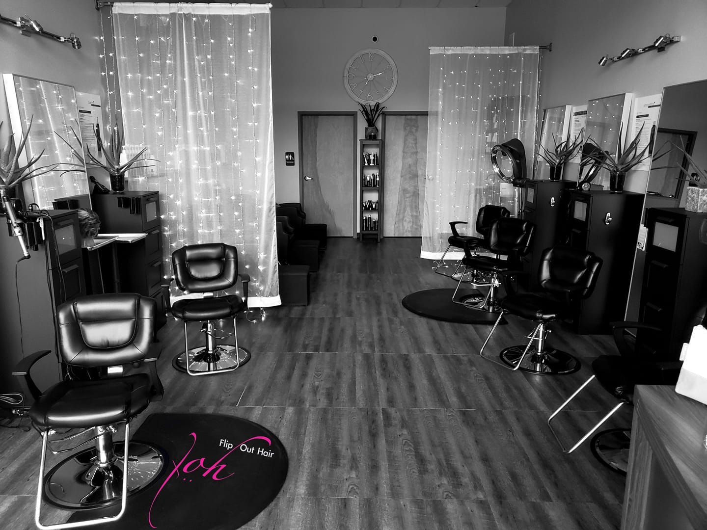 Interior of a hair salon with styling chairs, mirrors, and curtains. Wood flooring.