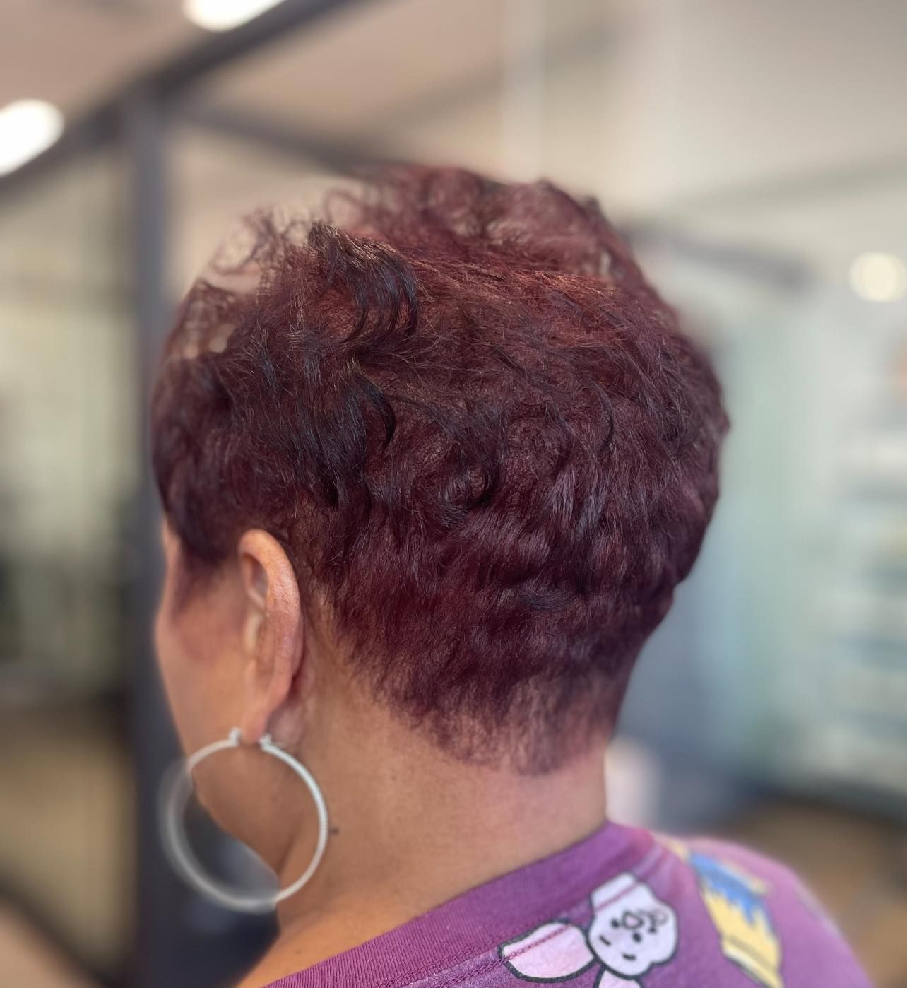 Woman with short, burgundy hair wearing hoop earrings and a purple top.
