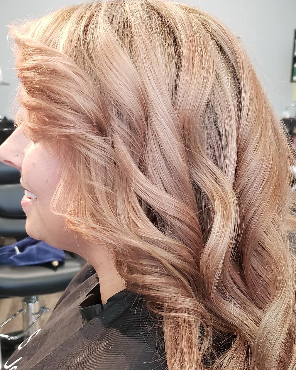 Woman with wavy, light brown and rose gold hair at a salon.